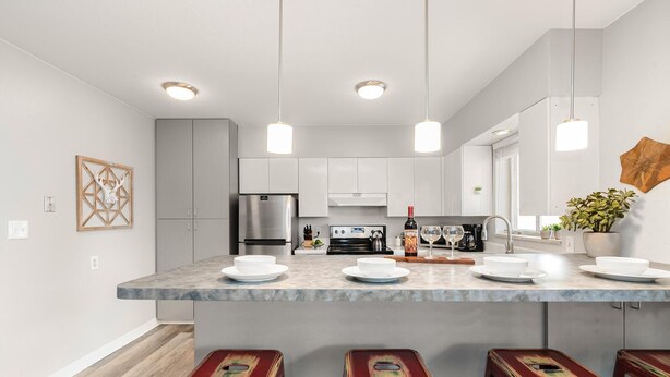 A modern kitchen with a central island, stainless steel appliances, pendant lighting, and a rustic decor piece.