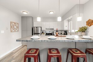 A modern kitchen with a central island, stainless steel appliances, pendant lighting, and a rustic decor piece. - Breathtaking condo in the heart of Old Town (Fort Collins)