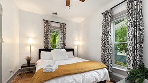 A bedroom with a bed, two bedside lamps, a window with curtains, and a plant on a nightstand. - Lola House! Cozy comfort, Prime Old Town Location (Fort Collins)