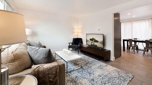 Ett modernt vardagsrum med en soffa, ett soffbord och en platt-TV. Det finns också en matplats med ett bord och stolar.