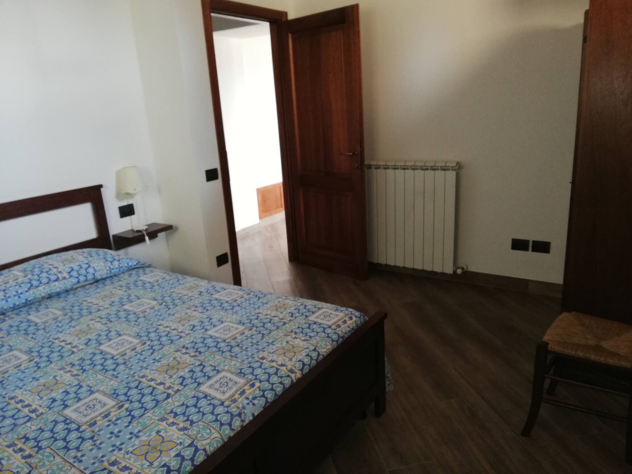 A bedroom with a bed, a chair, a radiator, and a wooden door.