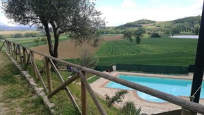 Une clôture en bois surplombe une piscine, offrant une vue sur un paysage verdoyant et des collines lointaines.