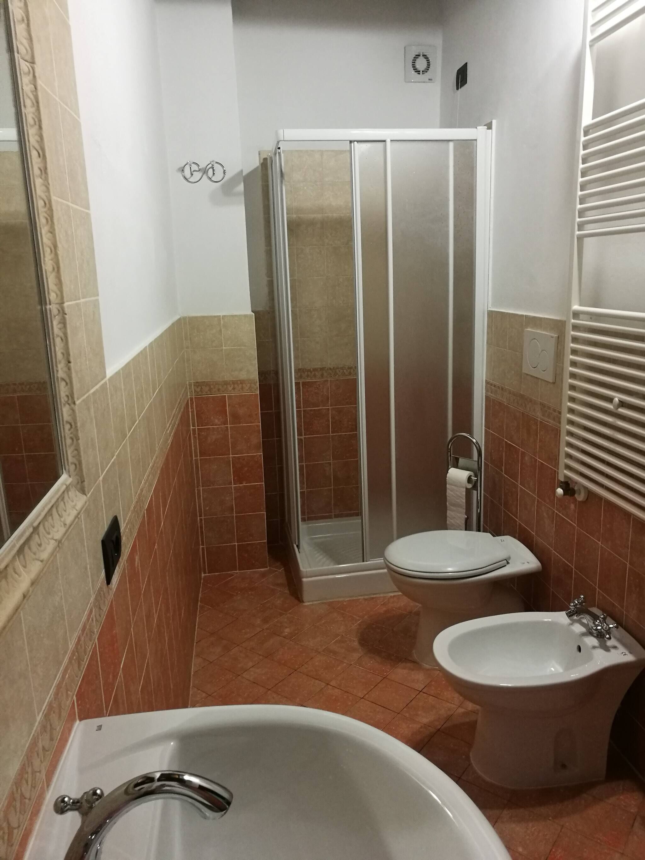 A bathroom with a bathtub, two toilets, a shower enclosure, and a towel rack.