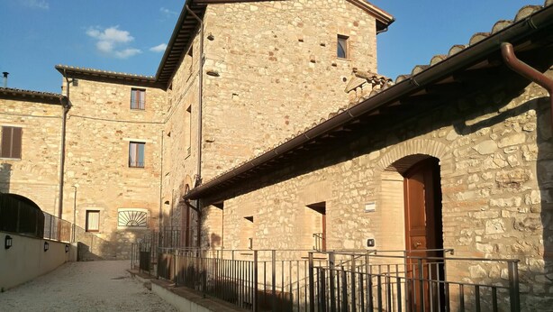 Un bâtiment en pierre doté d’une cour intérieure, avec une porte en bois et une rampe en métal.