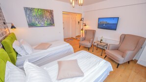 Een hotelkamer met twee bedden, een groene bank, een beige fauteuil, een kleine tafel met een lamp en een televisie aan de muur.