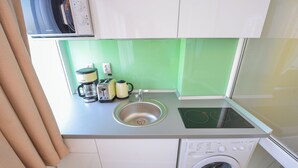 Een kleine keuken met een spoelbak, koffiezetapparaat, waterkoker en een wasmachine.