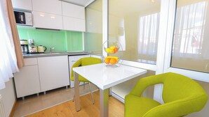 Een moderne keuken met witte kasten, een groene achterwand en een witte tafel met twee felgroene stoelen.