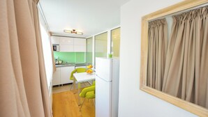 Een kleine keuken met witte kasten, een groen aanrecht en een eethoek met een witte tafel en twee groene stoelen.