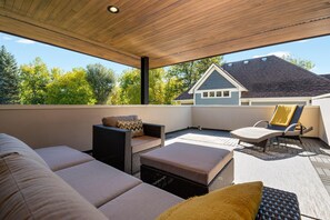 A covered outdoor seating area with wicker furniture and cushions, a view of a house in the background, and a clear sky. - Relaxing in Paradise w Private Roof Top Deck!! (Fort Collins)