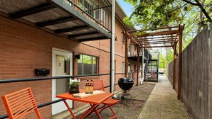 Een gebouw van baksteen met een terras, compleet met een tafel, stoelen en een barbecue. Een houten pergola biedt beschutting.