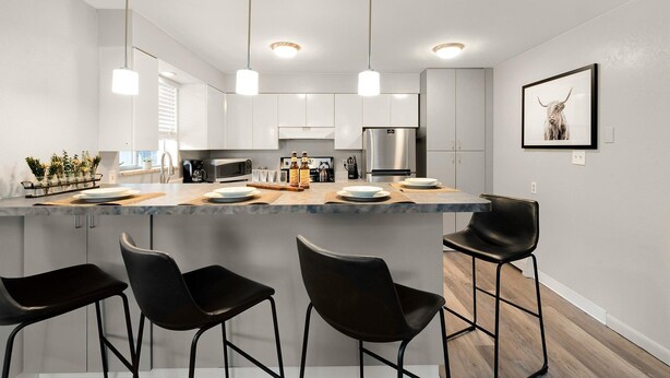 Een moderne keuken met een centraal eiland, barstoelen, roestvrijstalen apparatuur en hangende lampen.