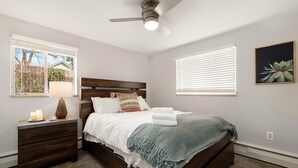 Een slaapkamer met een houten bed, een nachtkastje, een lamp en een plafondventilator.