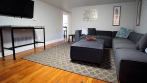 Un salon moderne avec un canapé gris, un pouf noir et un tapis à motifs.