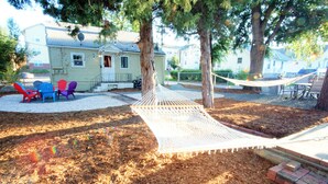 Un hamac tendu entre deux arbres, des fauteuils Adirondack aux couleurs vives et un chemin de briques menant à une maison.