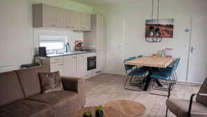 A modern kitchen with white cabinets, a dining area with a wooden table and blue chairs, and a brown leather sofa with a deer pillow.