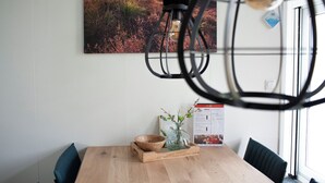 A dining area with a wooden table, a bowl, a vase with branches, and a hanging light fixture.