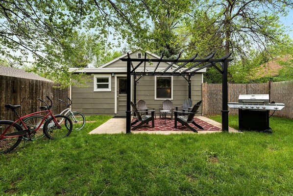 Relax in the backyard patio area, complete with a pergola, grill, and grassy lawn.