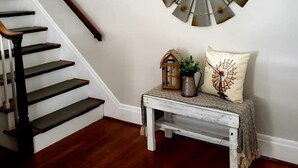 A staircase with dark wooden steps and a white wall. A decorative metal wall piece is mounted above a small table with a lantern, a vase, and a cushion. - Serenity in lancaster county (Paradise)