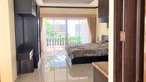 A bedroom with a bed, a desk, and a view of a balcony with plants.