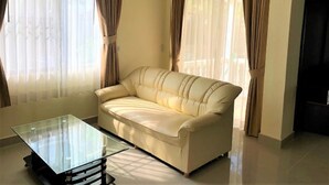 A living room with a beige sofa, a glass coffee table, and curtains on the windows.