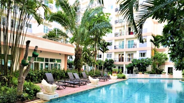 A swimming pool with lounge chairs and palm trees, surrounded by a multi-story building with balconies.