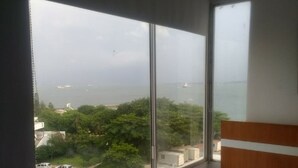 Een hotelkamer met een groot raam, met uitzicht op zee en een parkeerplaats.