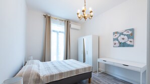 Een slaapkamer met een bed, een bureau, een kledingkast en een kroonluchter.