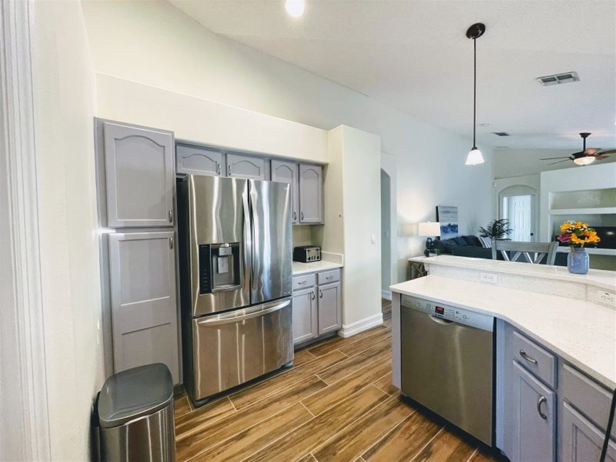 A modern kitchen with stainless steel appliances, wooden flooring, and light-colored cabinetry.