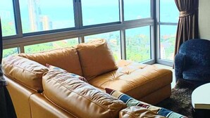 A room with a large window, a brown leather sofa, a blue chair, and a small white table. - 3110 - 2 Bedroom Seaview Deluxe Apt Unixx Pattaya (Pattaya)