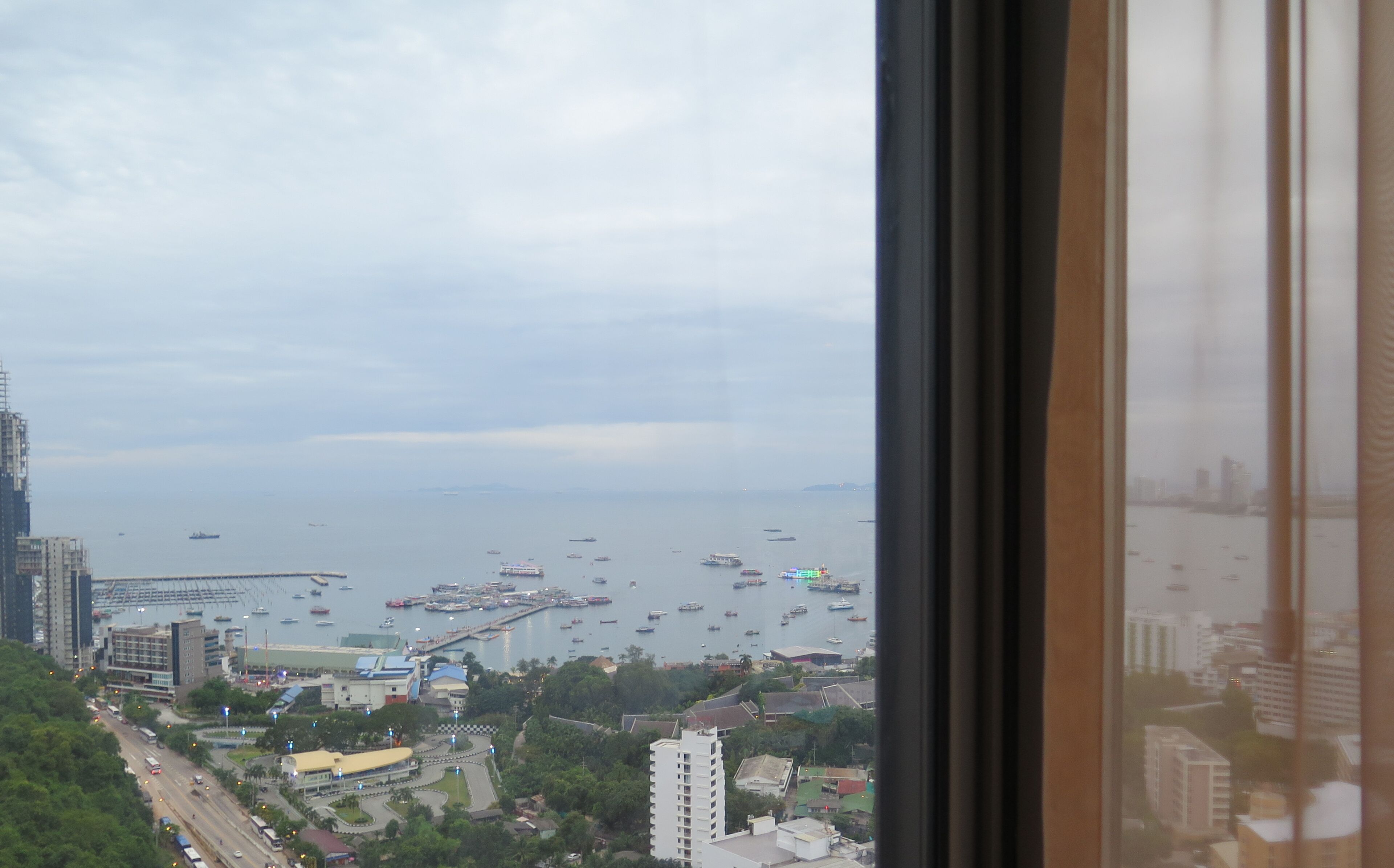 A coastal cityscape with a view of the sea and boats, buildings, and a road with vehicles.