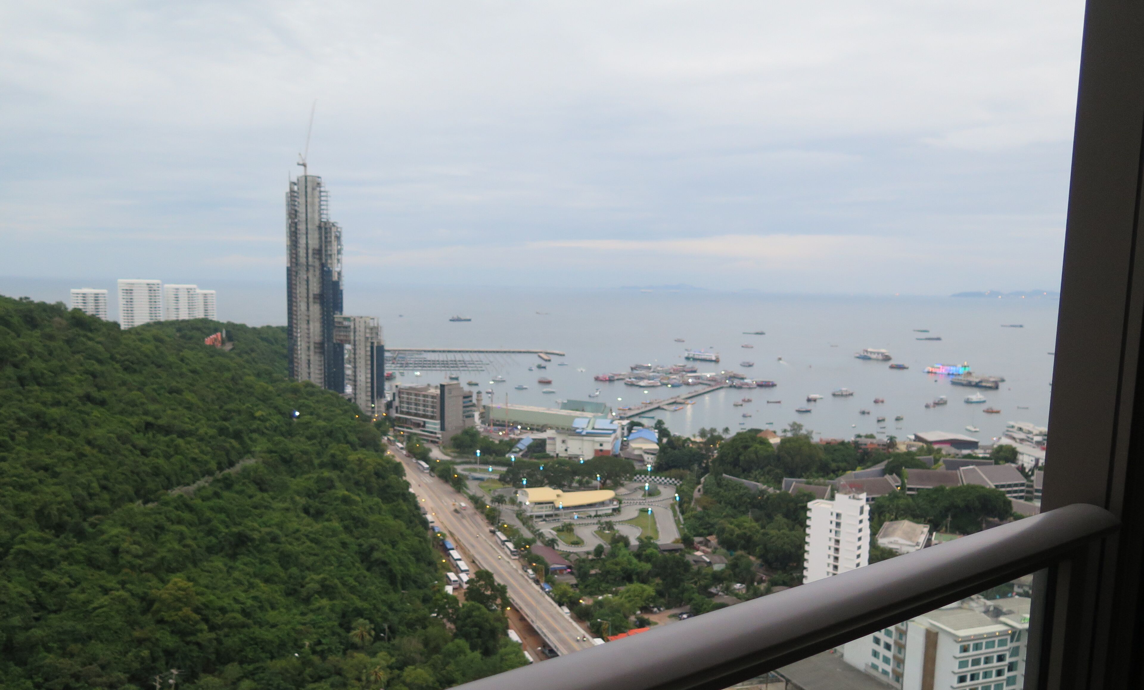 A coastal cityscape with a prominent skyscraper, a marina with boats, and lush greenery.