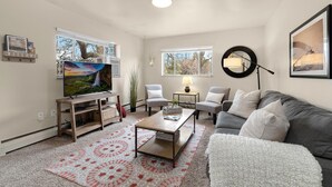 A living room with a TV, two chairs, a sofa, a coffee table, and a rug.