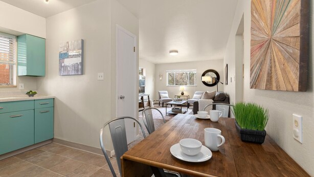 A modern kitchen with teal cabinets, a dining area with a wooden table, chairs, and a potted plant.