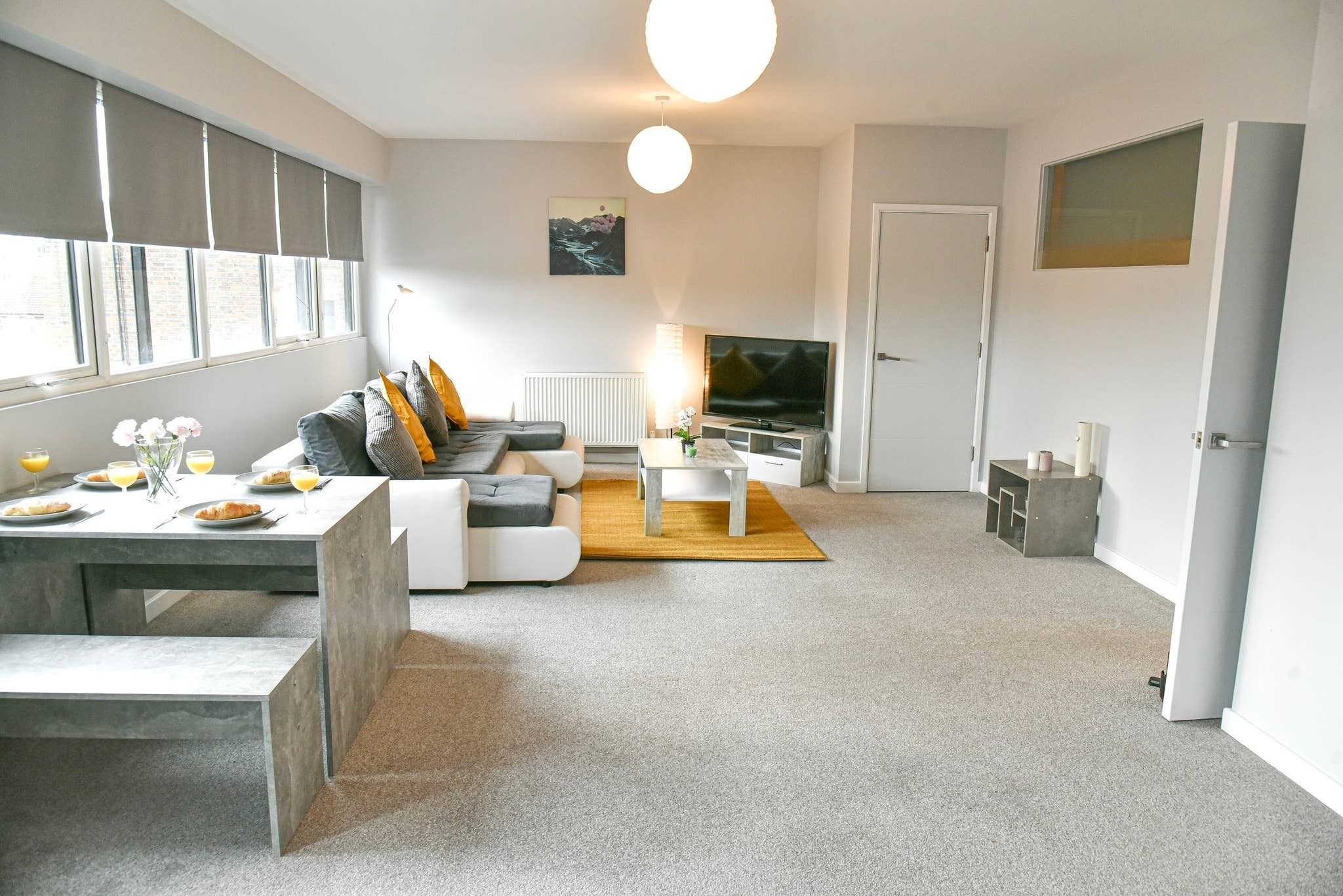 Ein modernes Wohnzimmer mit einer Couch, einem Couchtisch und einem Fernseher. Es gibt eine Essecke mit Tisch und Stühlen.