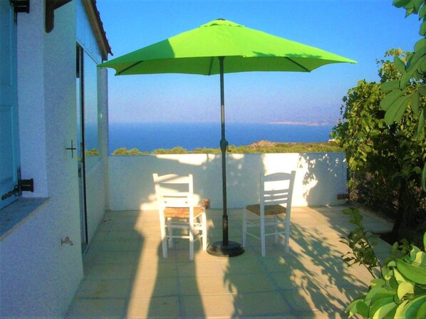 Relax in a serene outdoor seating area with ocean views, shaded by a green umbrella and surrounded by a white wall.