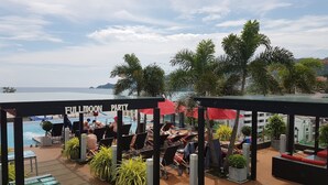 A poolside area with lounge chairs and umbrellas, a sign reading "FULLMOON PARTY", and a view of the sea.