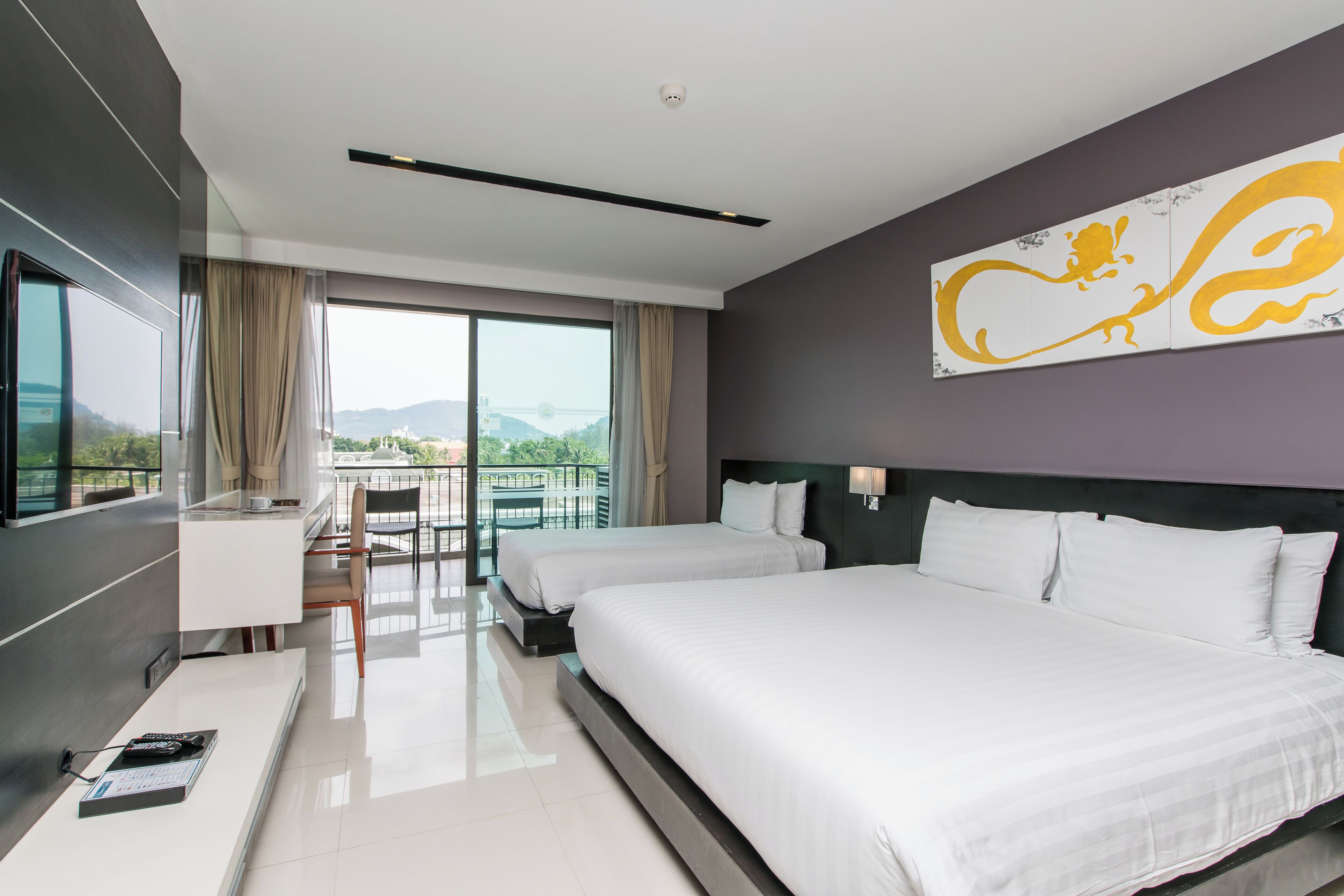 A modern hotel room with two beds, a desk, and a balcony with a view of the city.