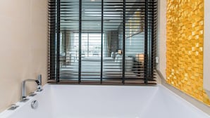 A modern bathroom with a large bathtub, a faucet, and a window with blinds.