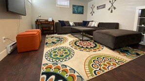 Un salon comprenant un canapé, un pouf, une table basse et un téléviseur fixé au mur.