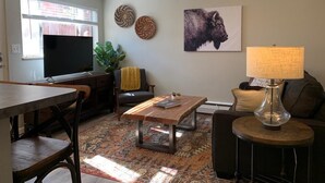 Ett vardagsrum med en platt-TV, ett soffbord, en soffa och en lampa.