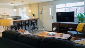 Ett modernt vardagsrum med en svart lädersoffa, ett träbord, en tv och en matplats med stolar och ett bord.