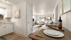 A modern kitchen with white cabinets, a dining area with a wooden table, and a living room with a sofa and chairs. - Contemporary condo in the heart of Old Town (Fort Collins)