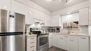 A modern kitchen with stainless steel appliances, white cabinetry, and a wooden floor. - Contemporary condo in the heart of Old Town (Fort Collins)