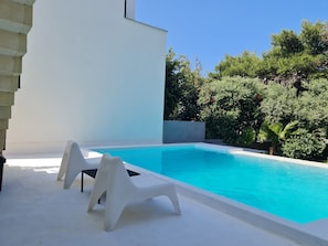 A swimming pool with white chairs and a white building in the background.