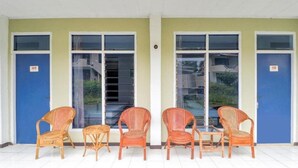 A row of wicker chairs and a small table outside a building with numbered doors. - OYO 3250 Setia Hotel (Cipanas)