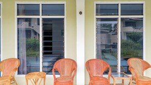 Un espacio exterior cubierto con asientos de mimbre y una mesa de vidrio, junto a amplios ventanales con vista a una zona residencial.