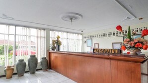 A reception area with a wooden reception desk, a 'RECEPTION' sign, and a window with blinds. - OYO 3250 Setia Hotel (Cipanas)