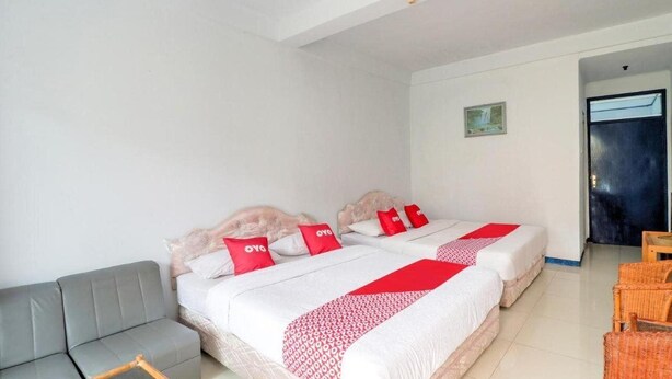 Habitación de hotel con dos camas, un sofá gris y sillas de mimbre.