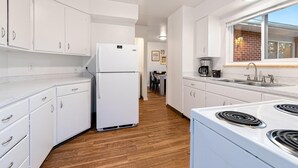 A modern kitchen with white cabinetry, a built-in stove, and a window overlooking a brick wall.