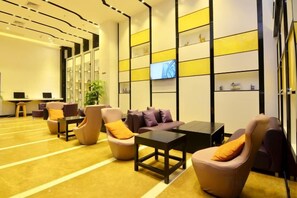 A hotel lobby with a reception desk, seating area with armchairs and sofas, a television screen, and a wall with shelves. - Lufeng Hotel (HuizhouLongmen) (Longmen)
